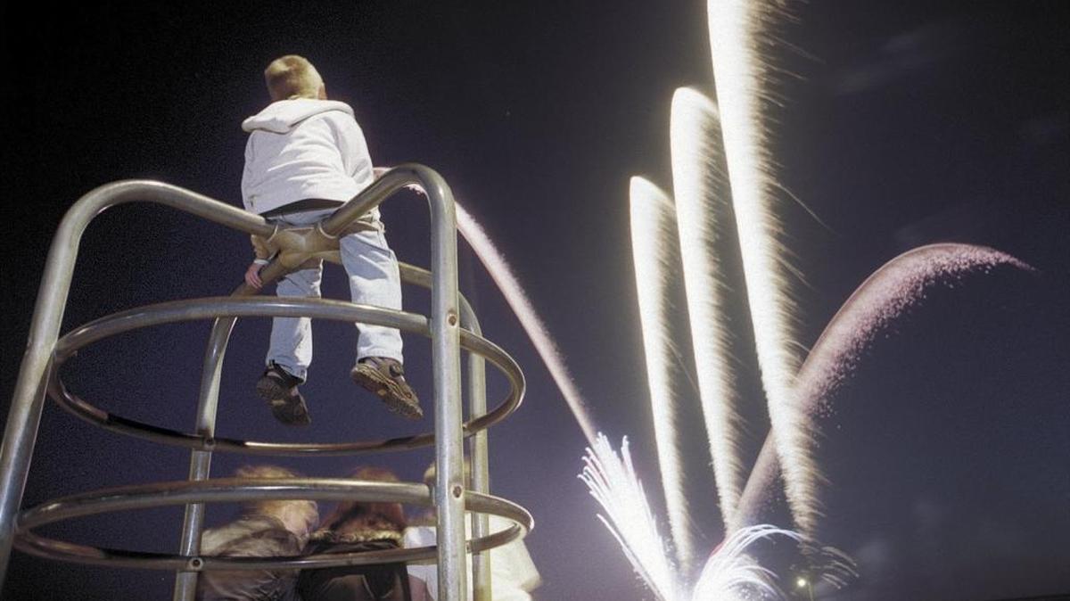 A young boy watches Fourth of July fireworks from the top of the monkey bars in Cayucos in 1999. The North Coast town will offer a scaled-down version of its fireworks show on July 4, 2021.