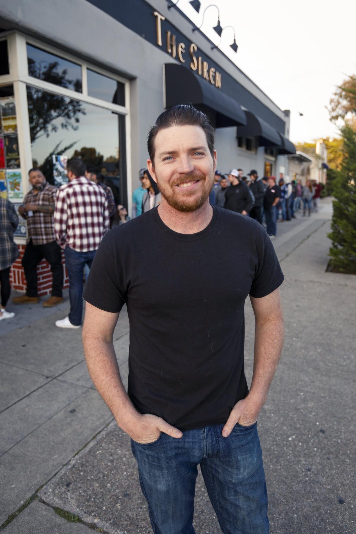 General manager Monte Schaller poses for a picture in front of The Siren, a former Morro Bay dive bar that's become a hot concert venue.  Behind him, concertgoers line up for a sold-out show featuring The Expendables.