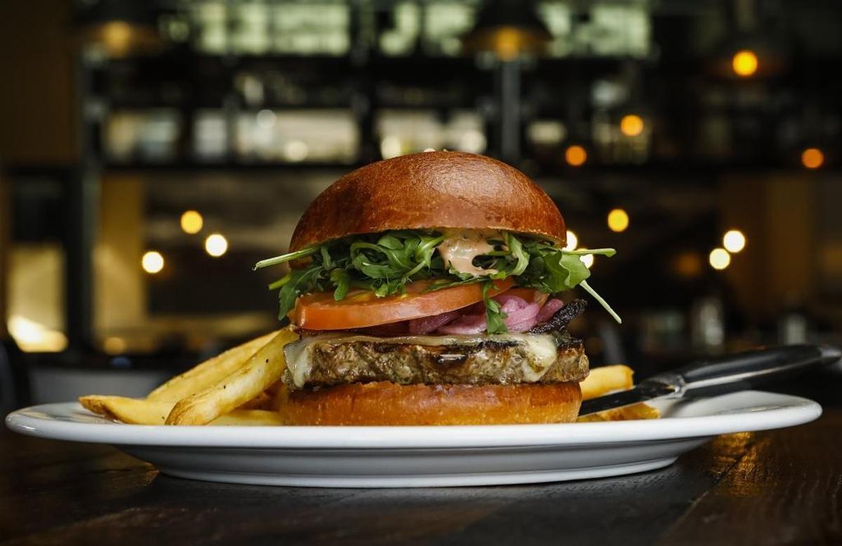 The Milestone Burger at Milestone Tavern in San Luis Obispo features half a pound of house-ground brisket, chuck and sirloin beef, plus house-cured bacon, Awiss cheese, house-pickled onion, tomato and arugula, on a brioche bun.