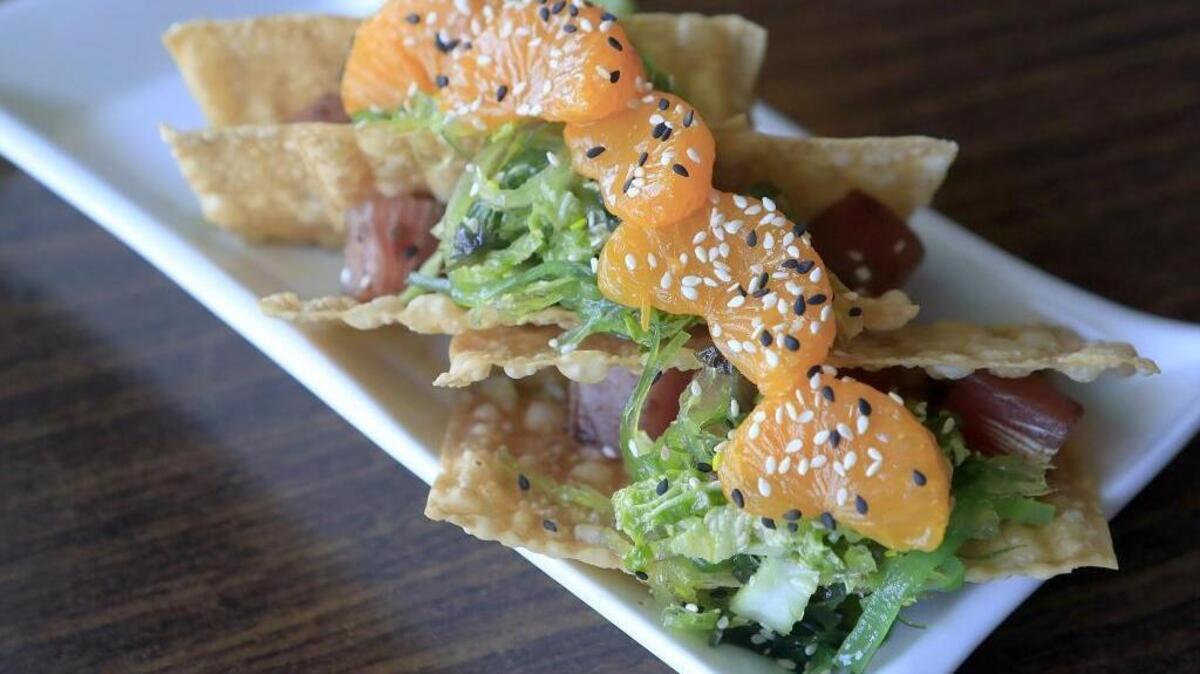 KunFusion sushi-grade ahi tuna tacos are served with wake seaweed slaw, mandarin oranges and sesame seeds in crispy egg-roll shell.