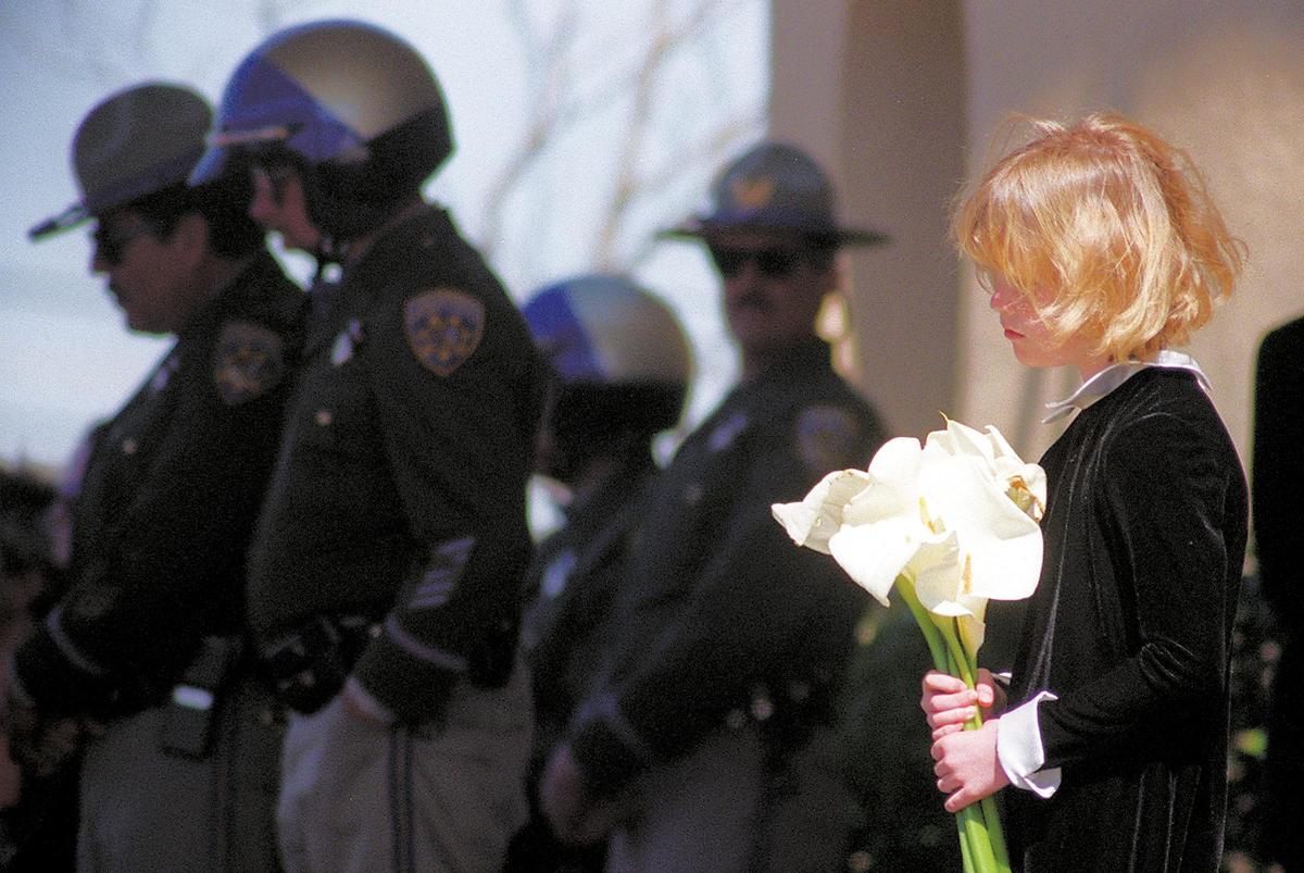 Catlin Haverty, 9, holds flowers as memorial service takes place March 1, 1998, for CHP officers Rick Stovall and Britt Irvine at the Pacific Christian Center in Santa Maria. The officers were responding to a late night call of a truck accident on Highway 166. The flood swollen Cuyama River had washed out the roadway. California Highway Patrol officers stand behind her. Haverty’s father was a doctor for one of the dead officers.