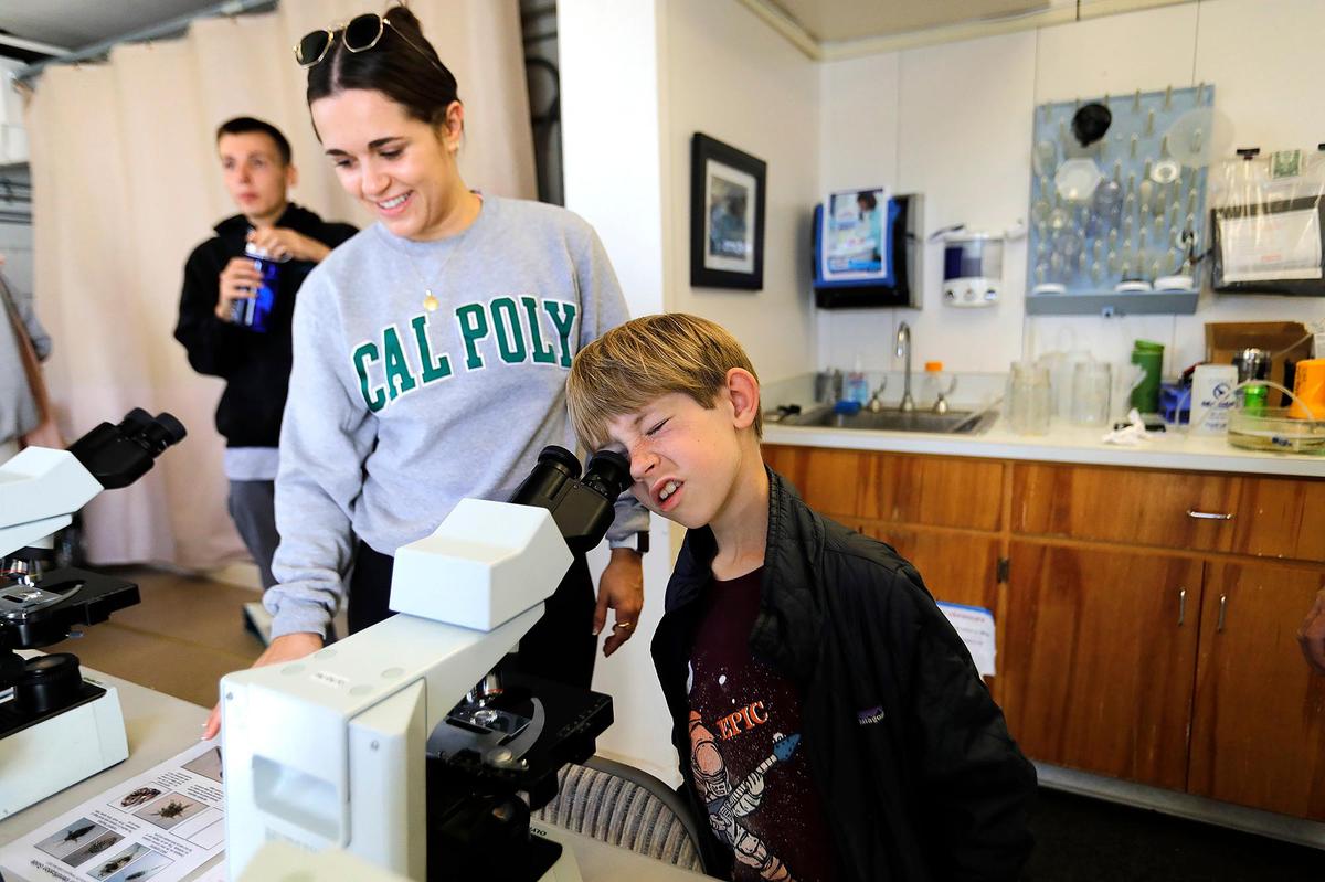 Caiden D’ Entremont , 8, of Atascadero looks through a microscope at plankton in sea water on Saturday, Oct. 29, 2022, during an open house event held at Cal Poly Pier in Avila Beach by Cal Poly’s Center for Coastal Marine Sciences. Eva Kokkino, Cal Poly biology major, helps him.