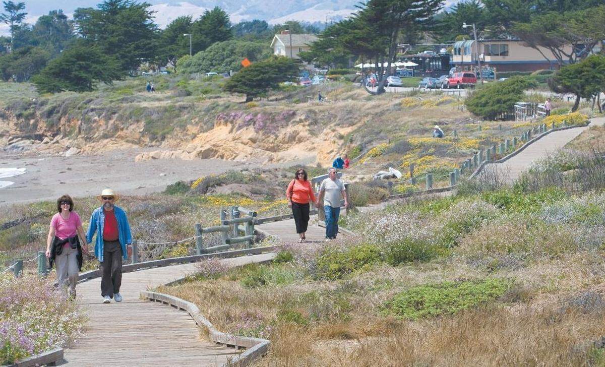 People walk along seashore on the Moonstone Beach Boardwalk in Cambria.