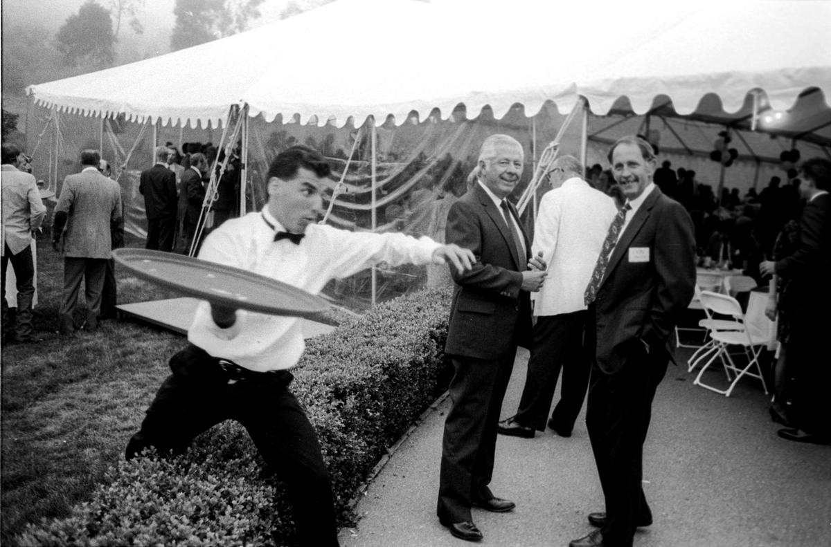 A waiter in a hurry hurdles a low hedge in front of guests Sheriff Ed Williams and rancher Don Talley at a dinner with Vice President Dan Quayle in Nipomo July 23, 1991.