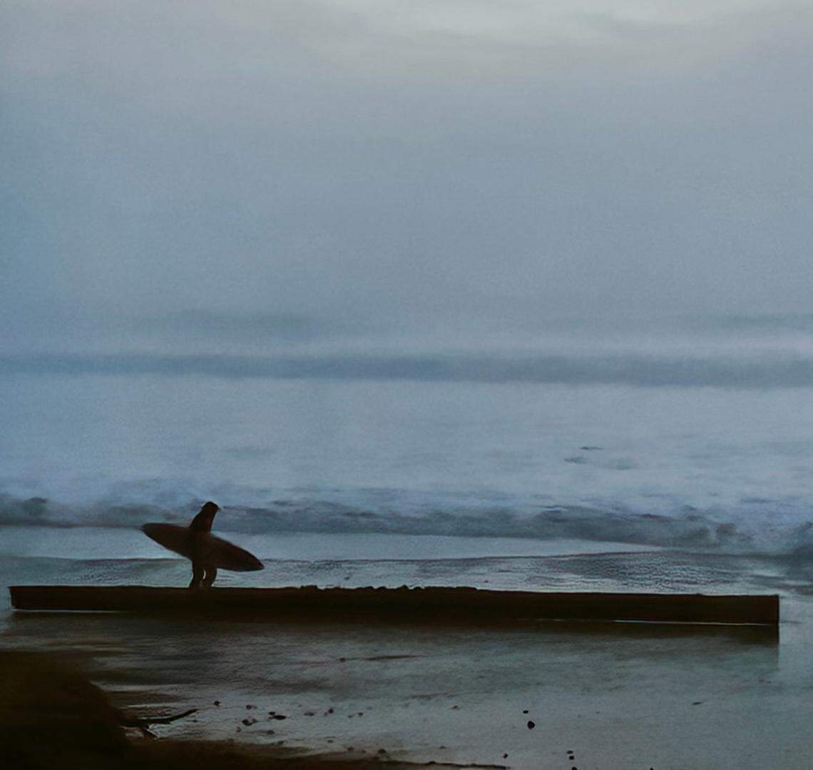 A surfer walks past a piling knocked loose from the Cayucos pier during a high surf event in December 2024.
