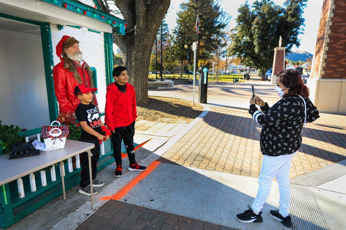 Carolina Arrastio of Paso Robles takes a photo of her sons Aron, left, 8, and Omar, 11, with Santa Claus, aka Charles Themens, on Saturday at the Downtown City Park.