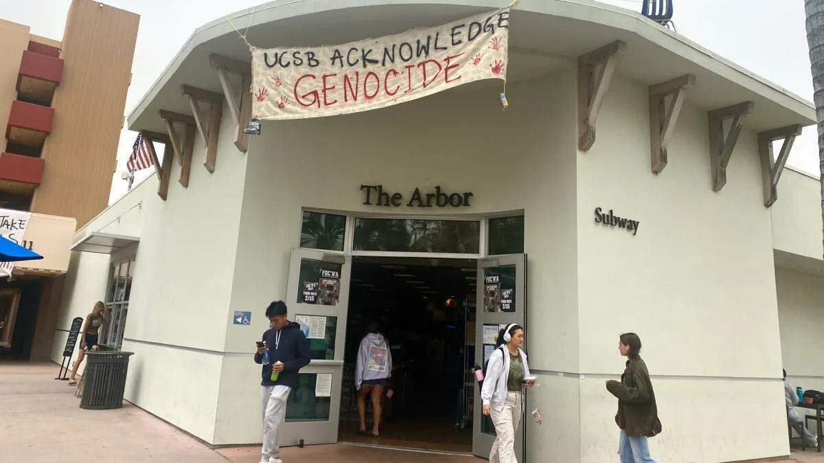 Pro-Palestine protesters use a sign above The Arbor on campus to call on UCSB to “acknowledge genocide.”  
