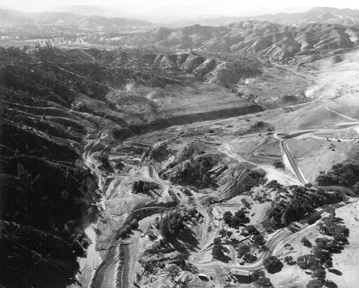NACIMIENTO DAM AREA... This aerial photo shows the site of the Nacimiento dam, being constructed where heavy equipment can be seen at the middle and left of the picture. Behind the dam can be seen the valley which the water will be backed up. Cleared areas to the left and right of the valley will be covered by water. The picture was taken by Clyde E. Plummer of Paso Robles.