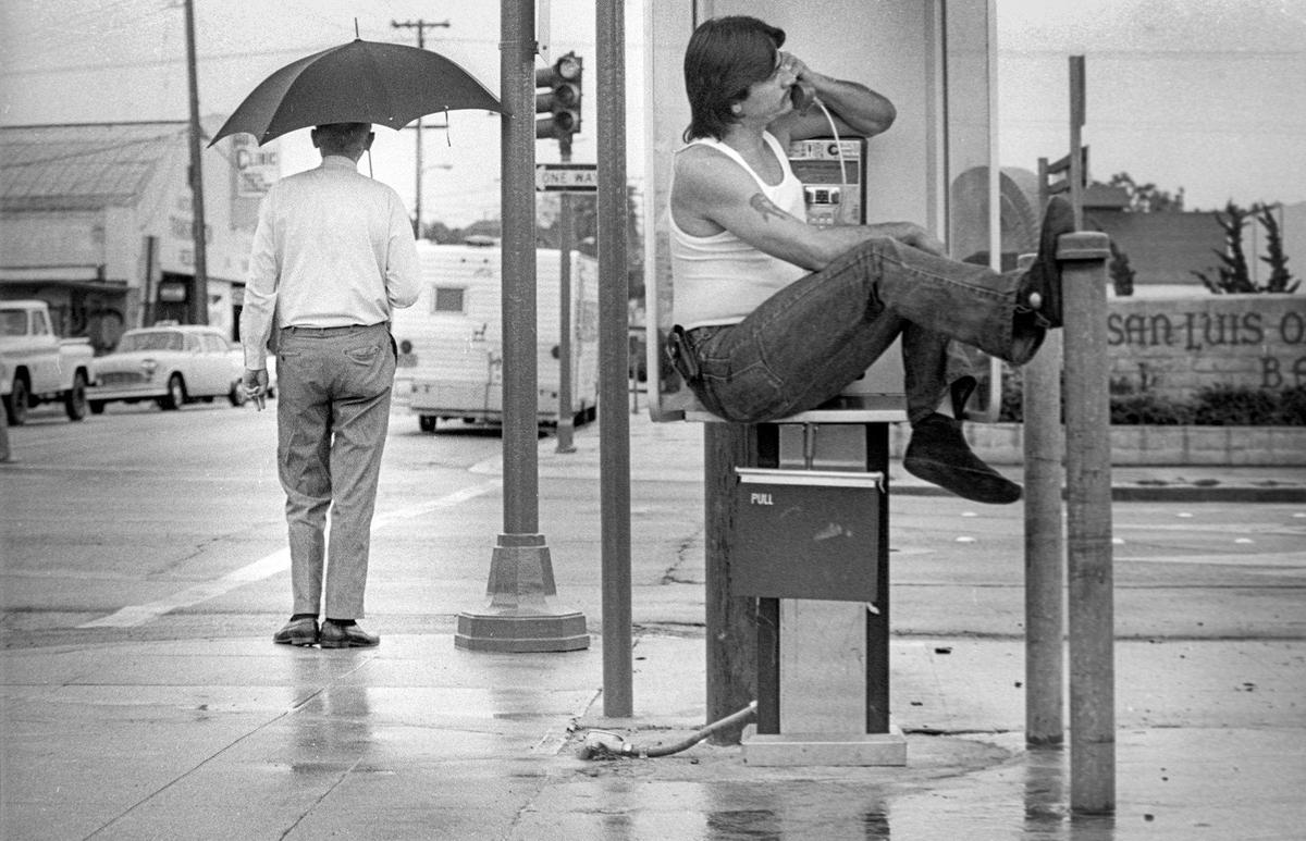 Floyd Ellis of San Luis Obispo propped himself on a telephone booth table on corner of Broad and Marsh streets in San Luis Obispo to avoid getting wet during showers from a tropical storm July 2, 1980.