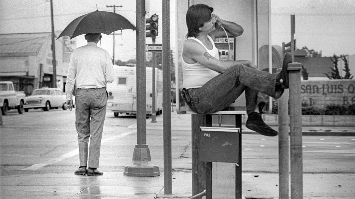 Floyd Ellis of San Luis Obispo propped himself on a telephone booth table on corner of Broad and Marsh streets in San Luis Obispo to avoid getting wet during showers from a tropical storm on July 2, 1980.