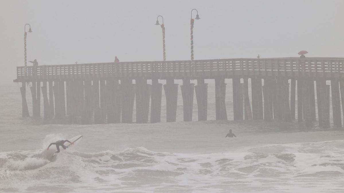 Surfers ply the waves in Cayucos during a rain storm on Tuesday, Jan. 27, 2022, as others watch from the pier. The National Weather Service issued a high surf advisory for beaches in San Luis Obispo and Santa Barbara counties.