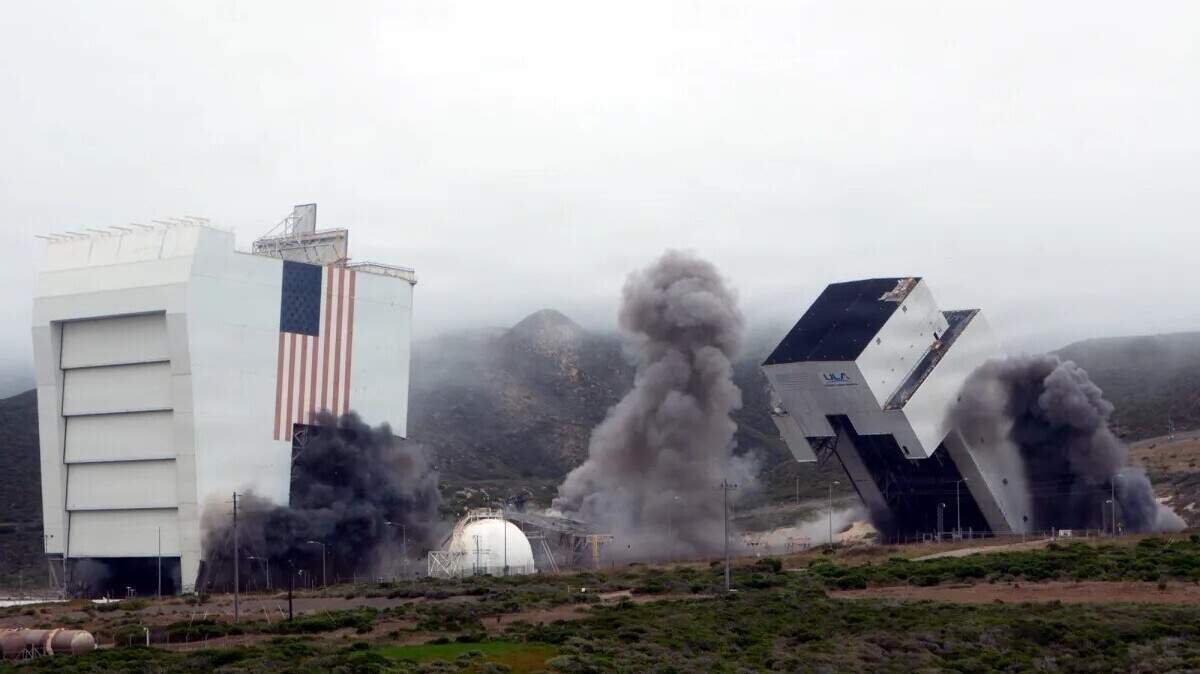 The mobile service tower, far right, collapses during a controlled demolition Tuesday, June 16, 2026, at Space Launch Complex-6 at Vandenberg Space Force Base. The fixed umbilical tower, center, fell already, and the mobile assembly shelter, left, rounded out the demolition.
