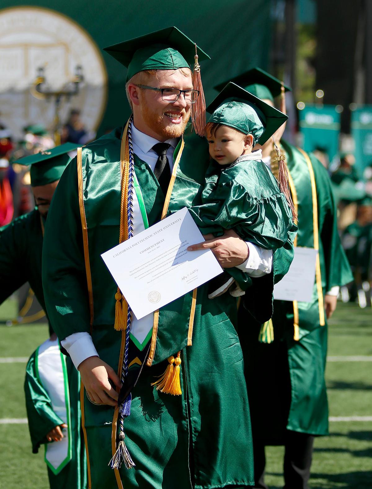 Several graduating students held a child in their arms. Caleb Sandberg holds his son 1-year-old Ezra. Cal Poly in San Luis Obispo celebrated the Class of 2025 with commencement ceremonies the weekend of June 14, 2025. The university’s six colleges had a total of 6,821 graduates.