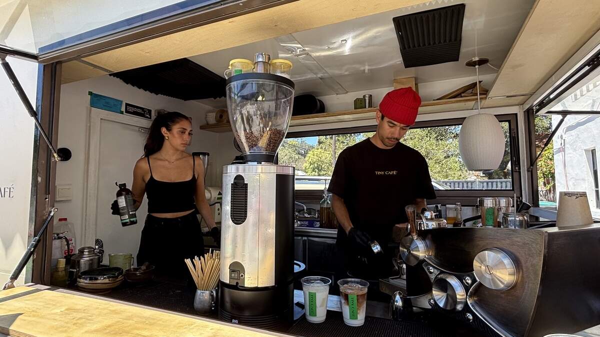 Co-owner of Tiny Café Colin Brown and an employee make drinks inside the mobile coffee trailer, using sustainable organic ingredients and compostable cups and straws, seen here on July 10, 2026.