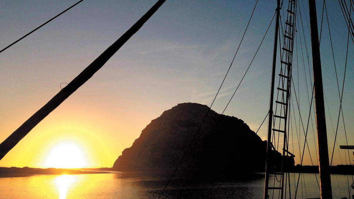 The sun sets behind rigging on a fishing boat, seen from the North T Pier in Morro Bay.