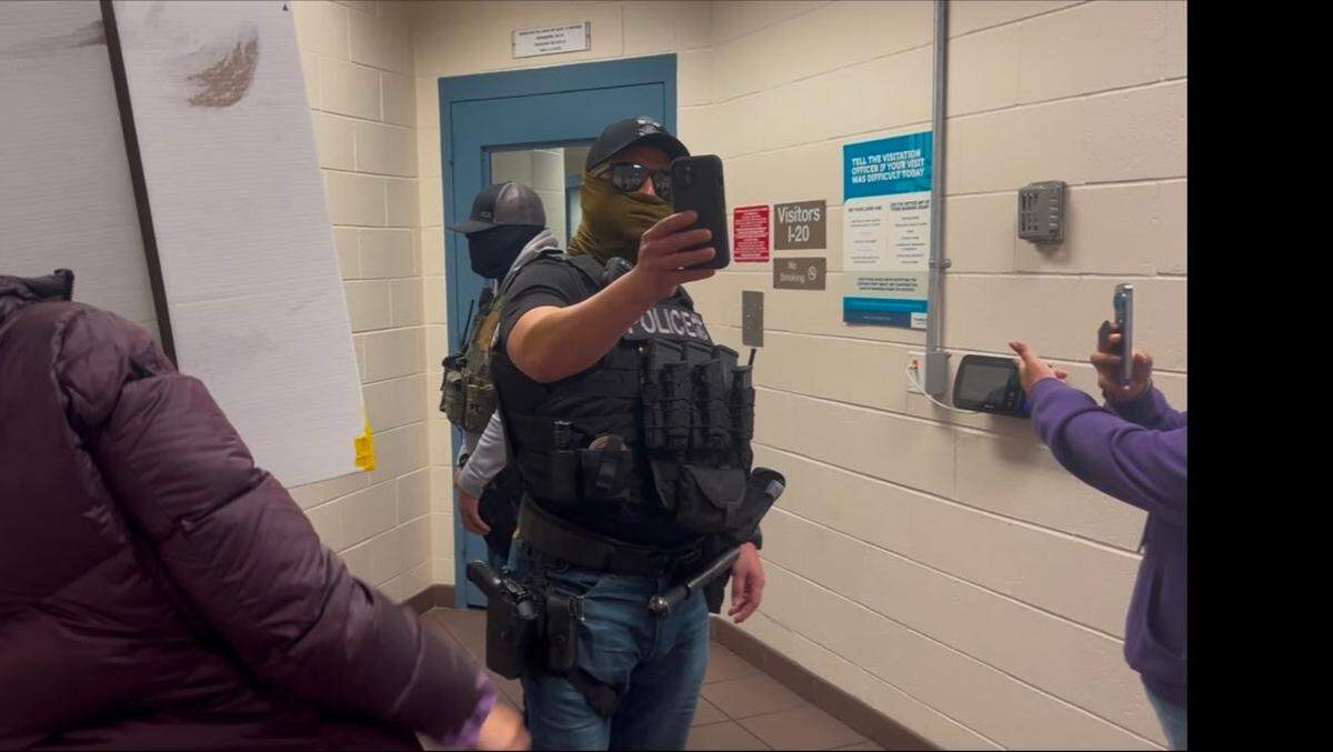 A U.S. Immigration and Customs Enforcement agent — wearing a mask, hat and sunglasses — takes a video of protesters in the San Luis Obispo County Jail lobby on Dec. 14, 2025.