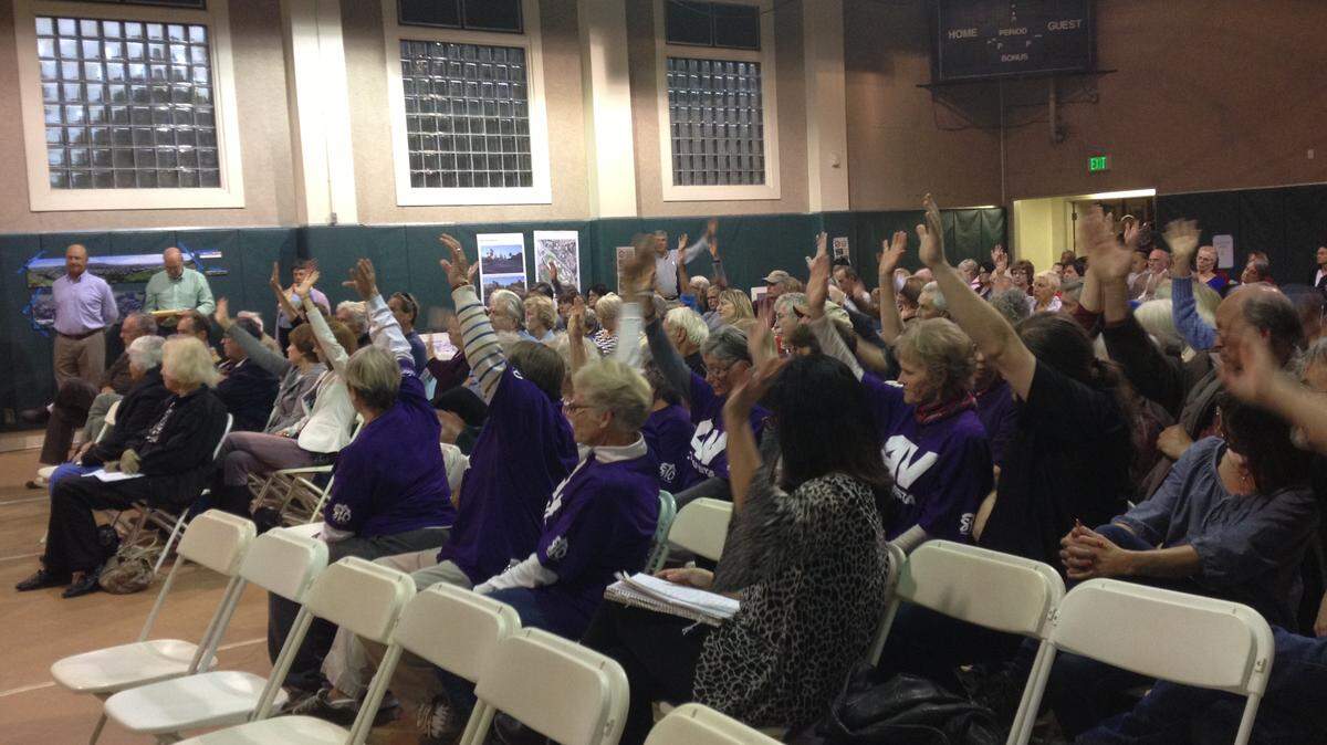 Residents at a San Luis Obispo City Council meeting raise their hands in agreement with a speaker criticizing a proposed dormitory complex at Cal Poly.