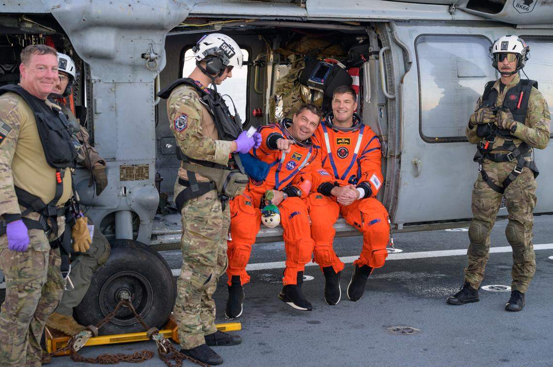 NASA astronaut Reid Wiseman, Artemis II commander, left, and CSA (Canadian Space Agency) astronaut Jeremy Hansen, Artemis II mission specialist, are seen sitting on a Navy MH-60 Seahawk from Helicopter Sea Combat Squadron (HSC) 23 on the flight deck of USS John P. Murtha after they were extracted from their Orion spacecraft after splashdown, Friday, April 10, 2026, in the Pacific Ocean off the coast of California.