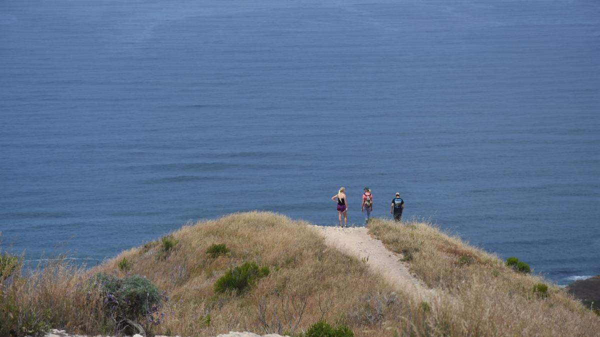 Hikers look out over calm ocean waters from a dune at Montana de Oro State Park.