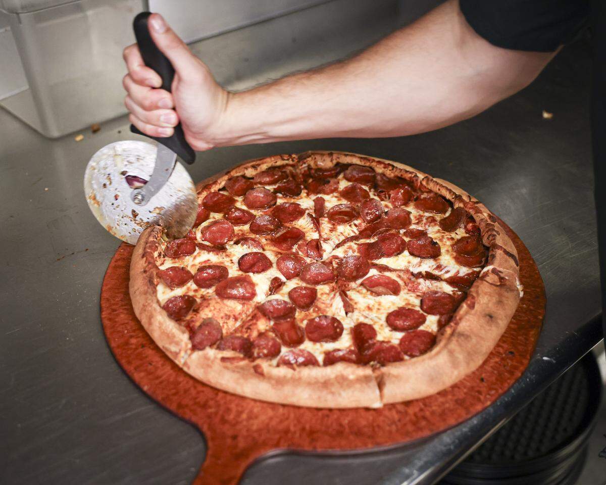 A pepperoni is sliced up for sale at the lunch counter. Woodstock's Pizza has been a downtown destination for casual dining for four decades, seen here on April 16, 2026