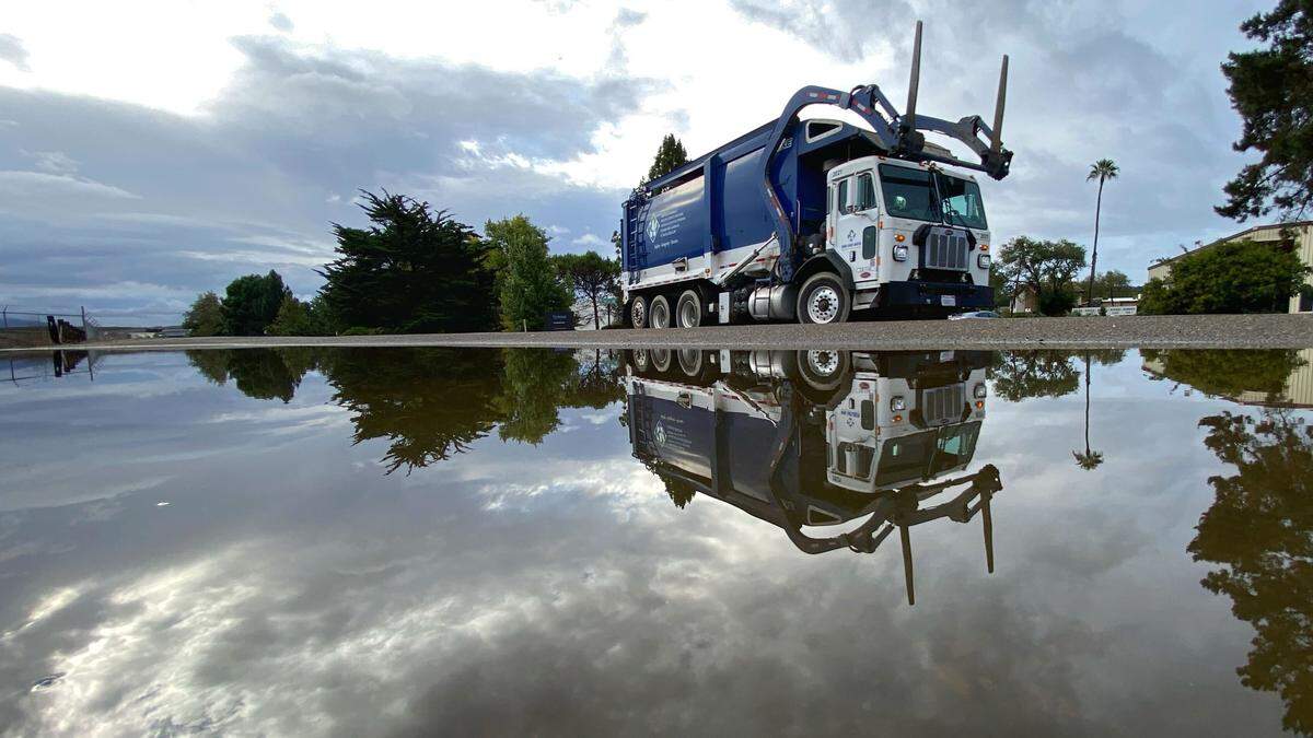 A garbage truck reflects in a puddle on Buckley Road near the airport on Oct. 14, 2025.