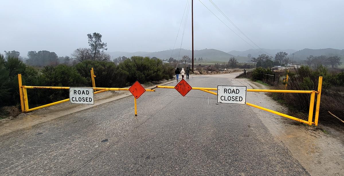 Prople walked past the Halcon Road closure barrier. The Salinas River in Atascadero is flowing causing the road to be closed, before the approaching “bomb cyclone” storm.
