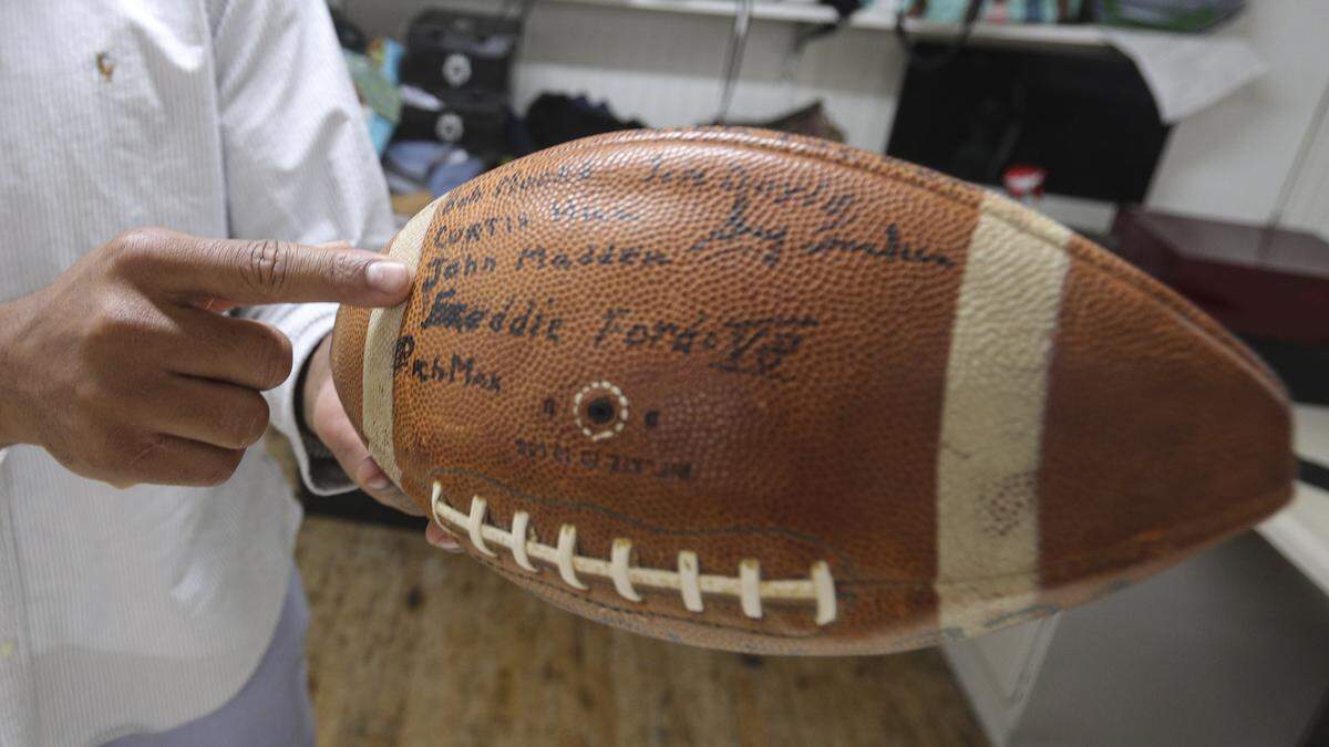 Thrifty Beaches co-owner Adam Kemp shows a Cal Poly team football with John Madden's name on it, seen on Sept. 3, 2025.