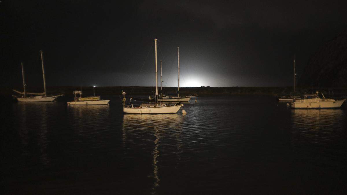 Lights from fishing boats beyond the sand spit light the night horizon as boats at anchor face the incoming tide in Morro Bay, seen here on July 30, 2025.