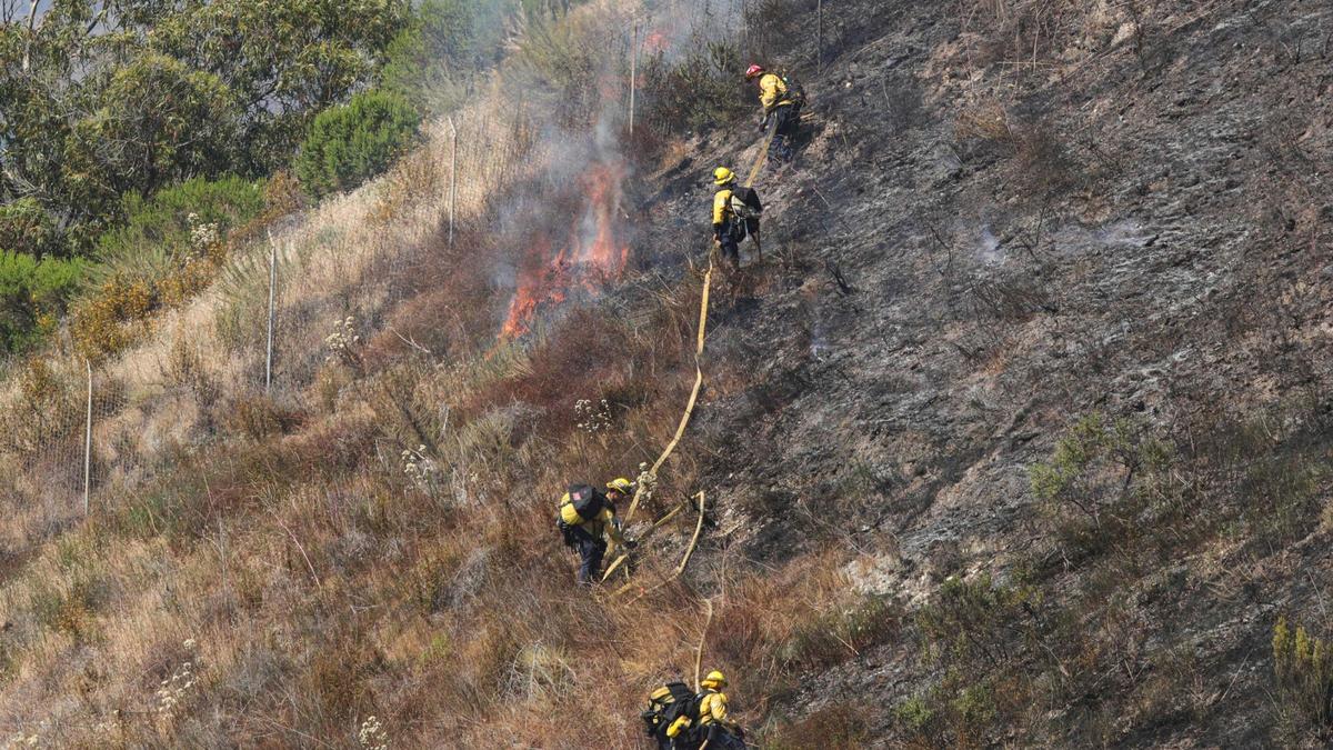 Firefighters pull a hoseline into position on a steep hill. They responded to a wildland blaze on the edge of Pismo Beach on June 9, 2025.
