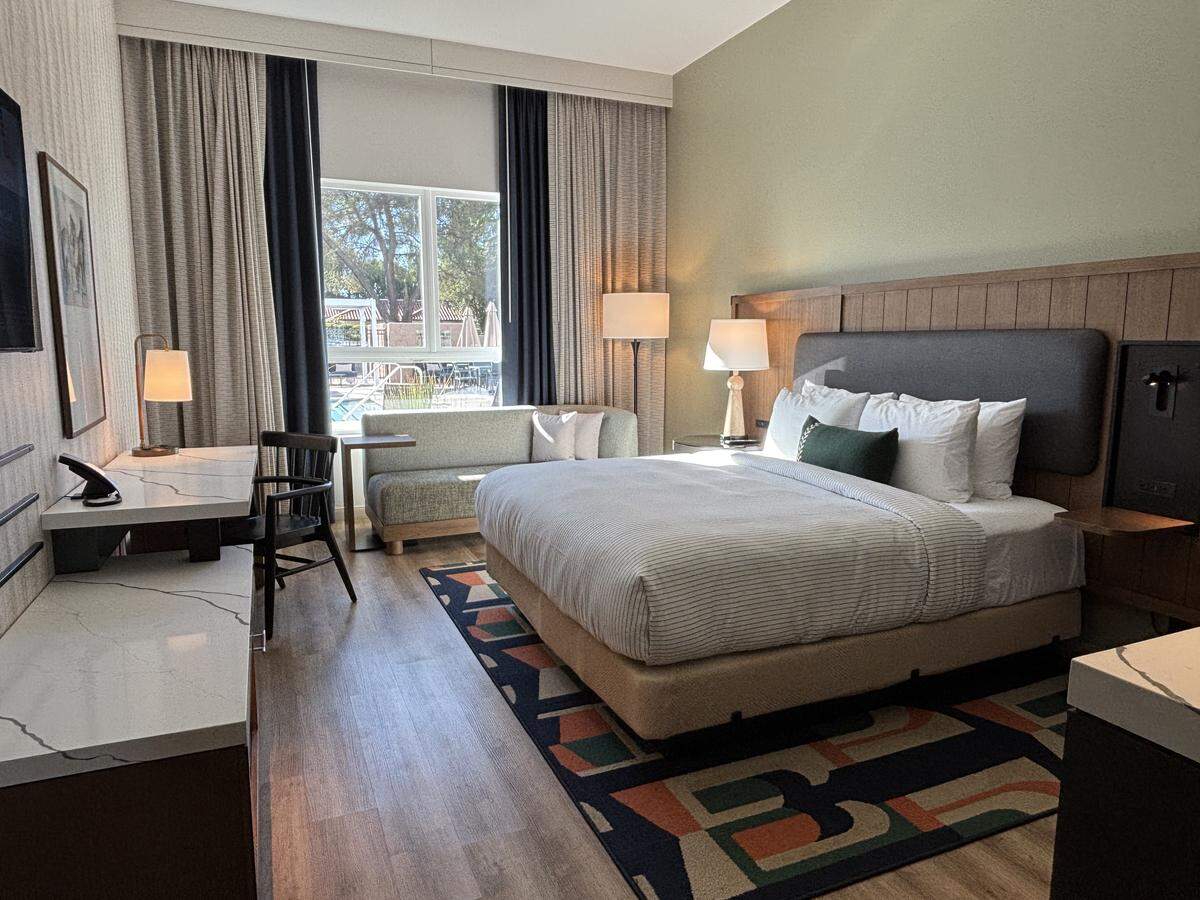 The hotel rooms at Cambria Hotel Templeton-Paso Robles have soft lighting from lamps and green accents from decorative pillows and one painted wall.