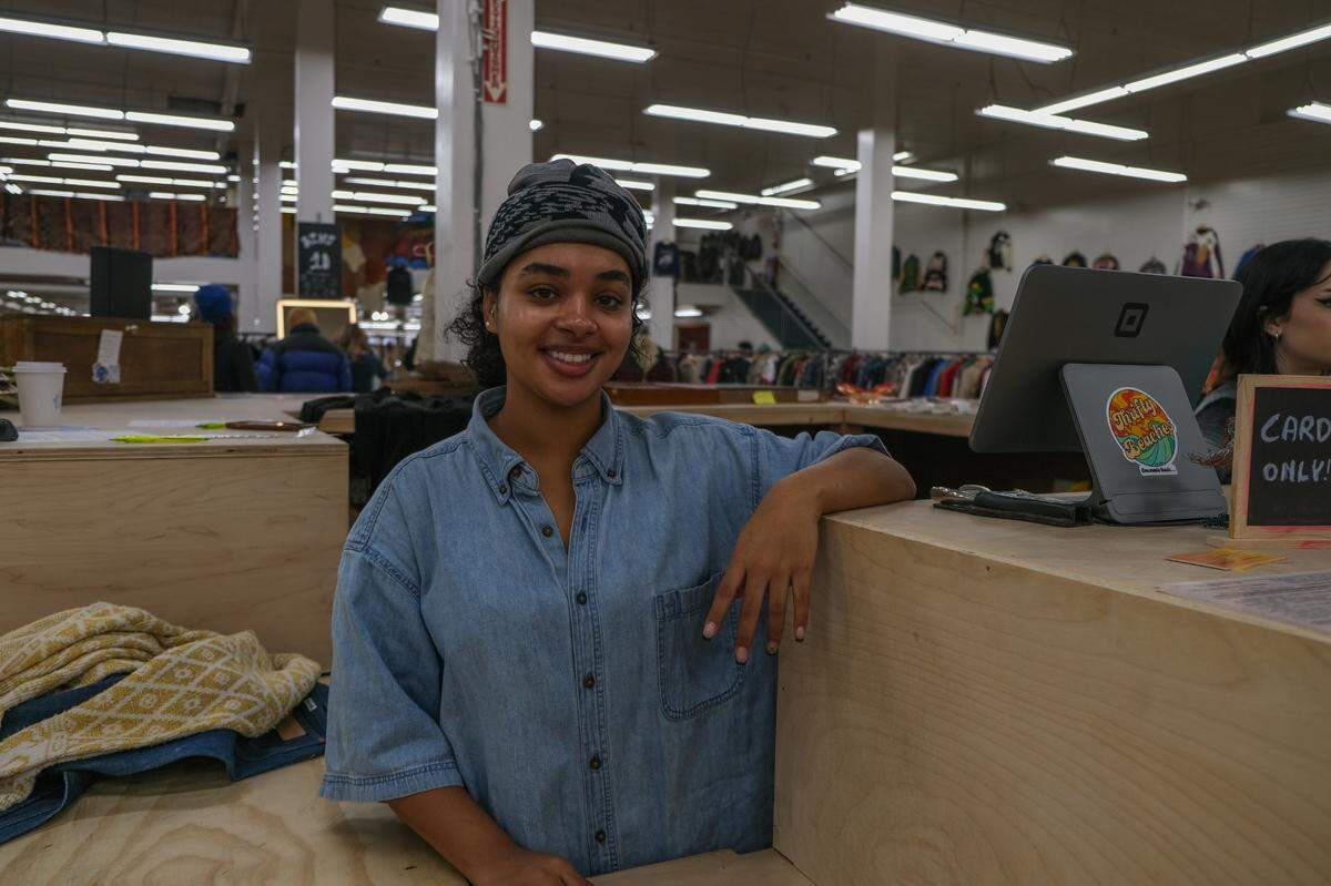 Thrifty Beaches co-owner Maria Trott poses at the cash register of her vintage clothing store, Thrifty Beaches, on Black Friday, Nov. 29, 2024.