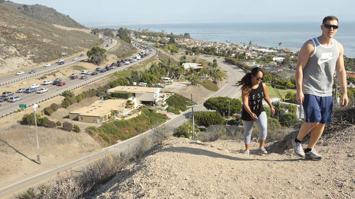 Naomi Kelly and Steve Vizzusi hike the hill carved to make way for Highway 101 in Shell Beach. Rush-hour congestion can be seen in the southbound lanes below.