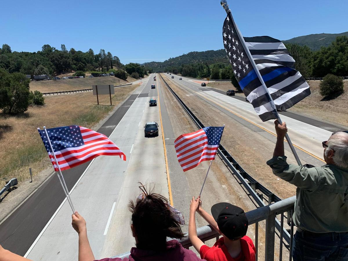 Corrin Lee, her son Blake Lee, 8, and Ray Gould wave flags as the procession for San Luis Obispo police Det. Luca Benedetti drives beneath the Santa Barbara Road overpass in Atascadero following Thursday’s memorial.