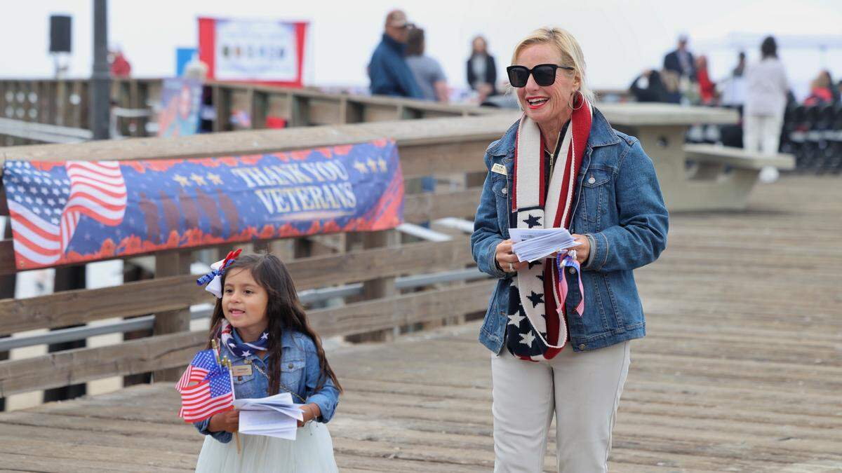 Georgie Ramos, 5, and Denise Wasson hand out programs at Pier on behalf of Pismo Beach Chamber of Commerce during its Veterans Day ceremony on Nov. 11, 2025.