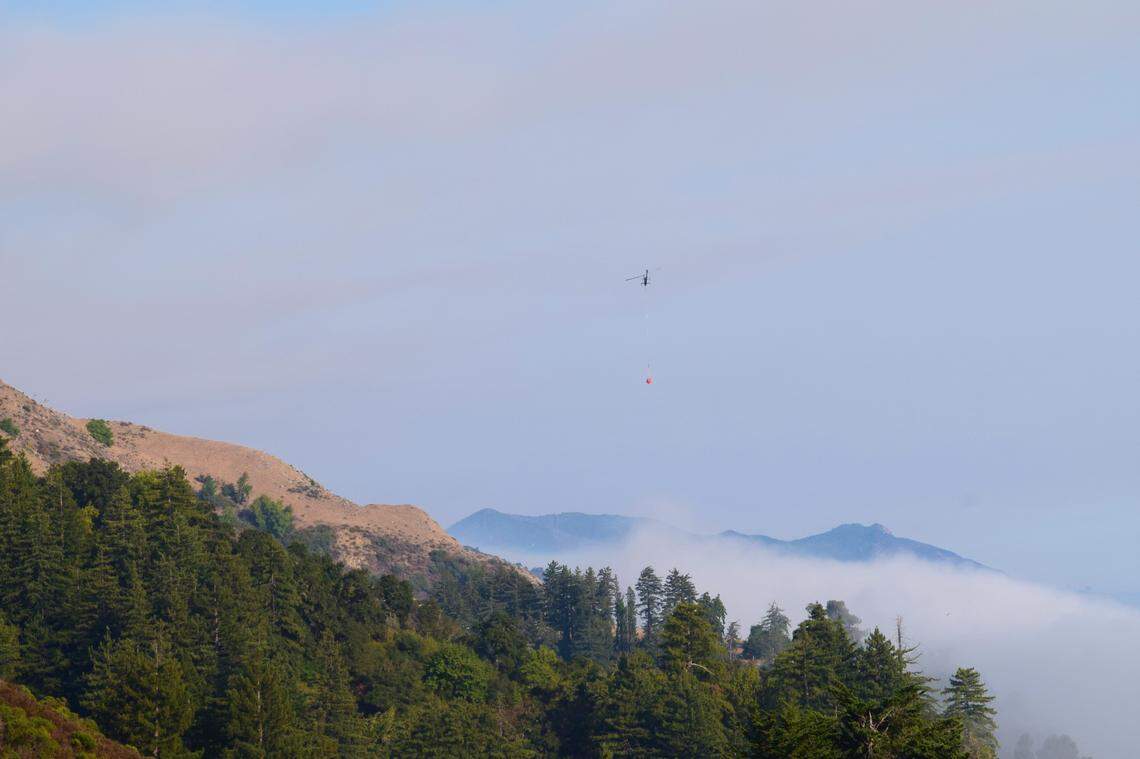 A helicopter carrying water to fight the northern edge of the Dolan Fire near Big Sur flies over fog and through smoke.