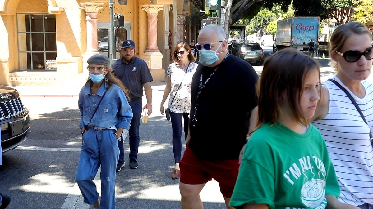 Masked and unmasked people cross the street at Chorro and Higuera on the first day of California’s full reopening in San Luis Obispo.