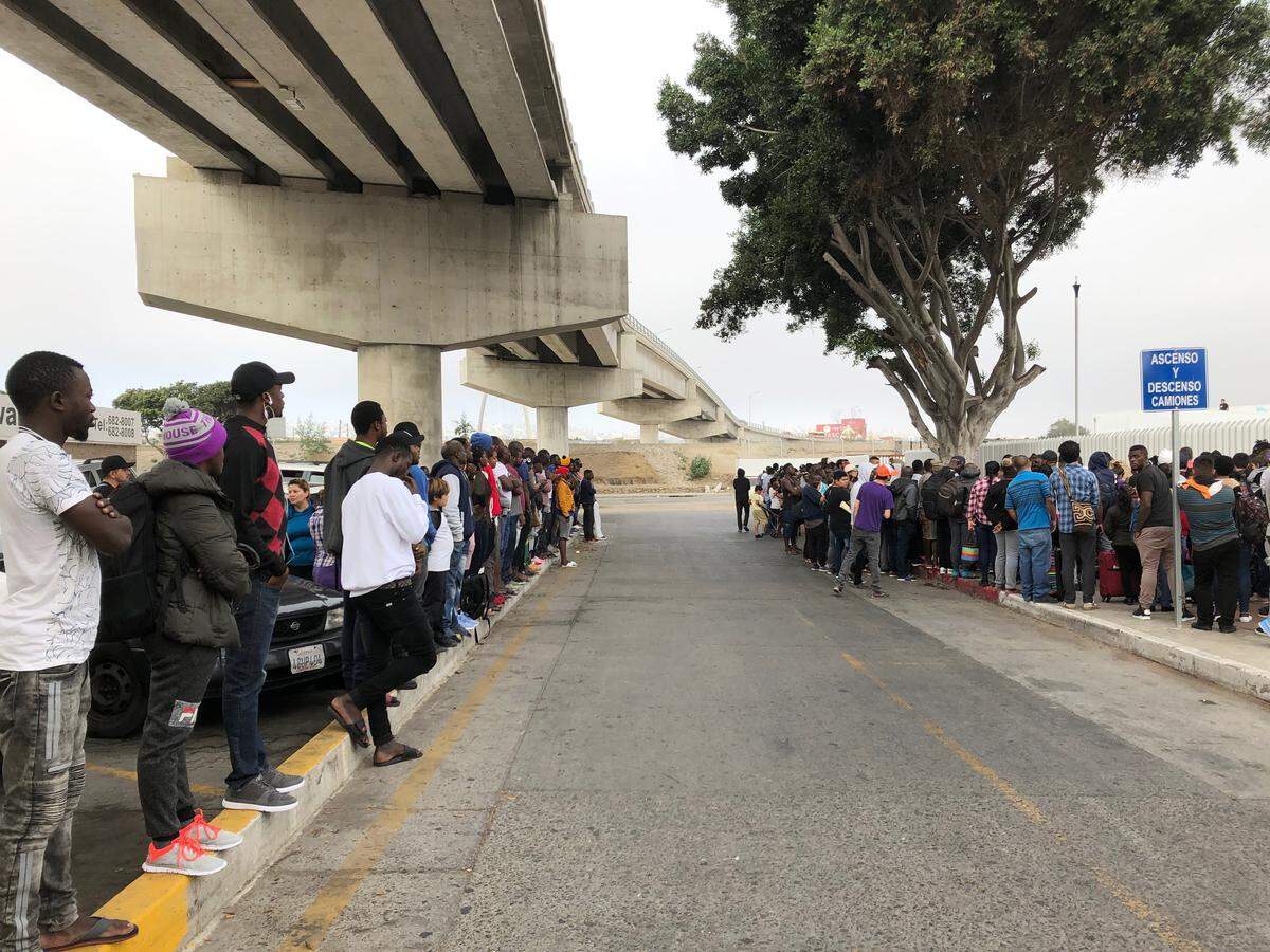 In this July 26, 2019 photo, a group of migrants in Tijuana, Mexico, listen to numbers being called for people to claim asylum in the U.S. The long waits are starting to test the patience of immigrants and border towns.