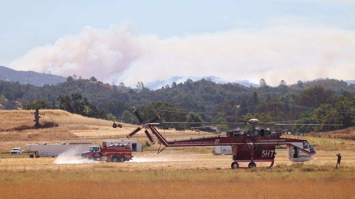 A helicopter prepare for takeoff at the base at Santa Margarita Ranch as smoke from the Gifford Fire rises in the background on Wednesday, Aug. 13, 2025.