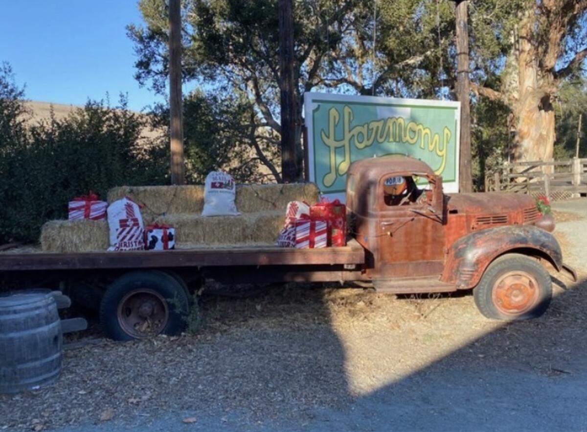 A red truck carrying hay bales and wrapped gifts is parked next to a Harmony sign.