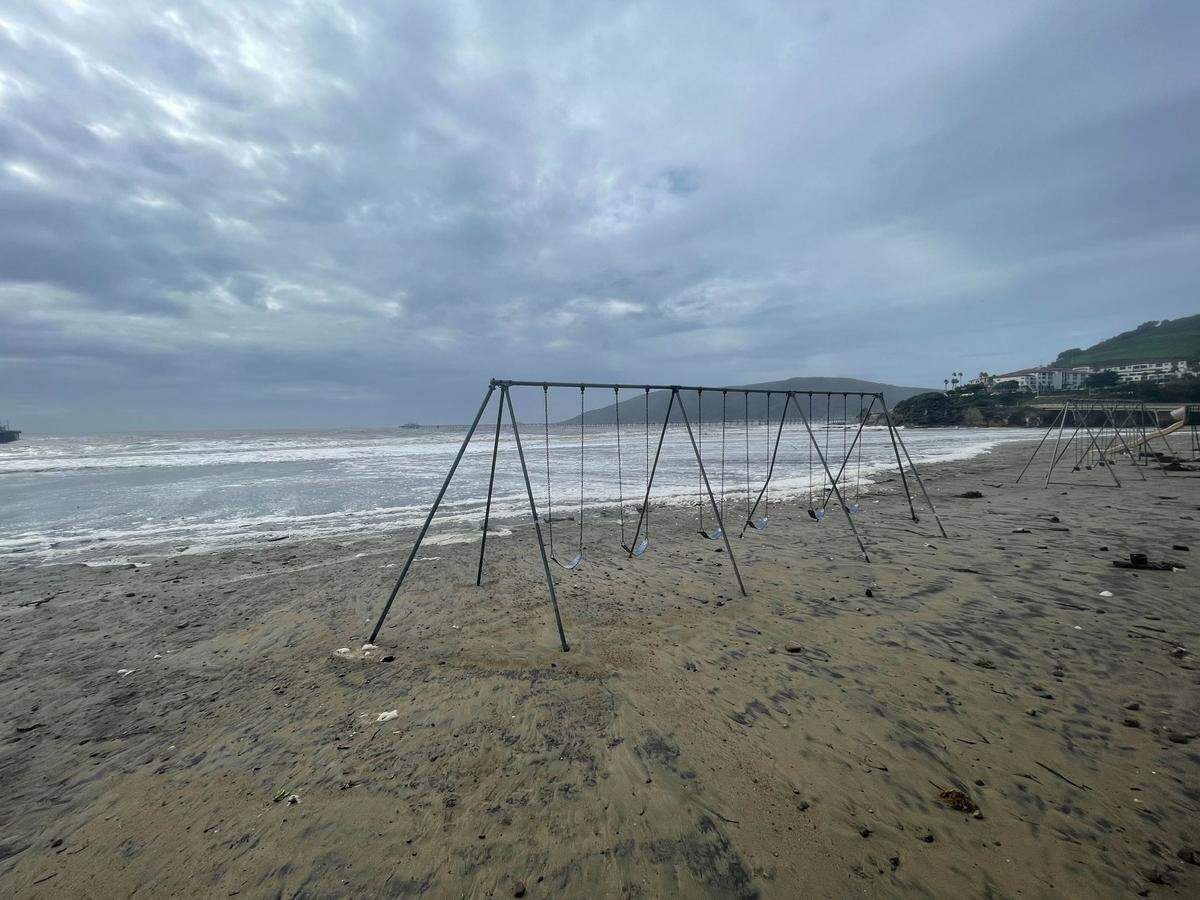 Seafoam, seaweed and other storm debris litter the sand near a shoreside swing set in Avila Beach on Thursday, Jan. 5, 2023, following a powerful winter storm.