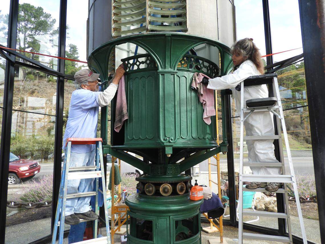 Volunteers Abel Martinez and Holly Gant clean the exterior cabinet of the Piedras Blancas Lighthouse’s 147-year-old Fresnel lens, which has been on display in downtown Cambria since 1996.