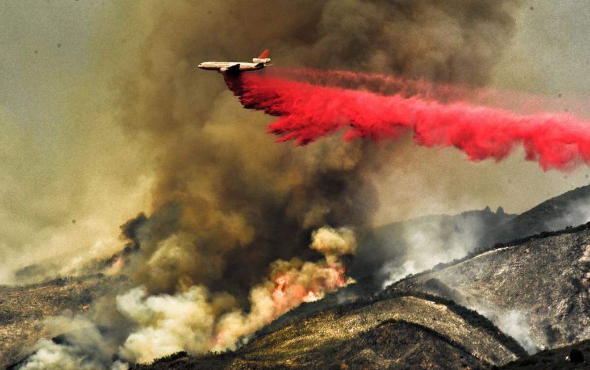 A DC-10 aircraft makes a phos-chek drop near flames above Highway 154 as firefighters battle the Cave Fire on Tuesday.