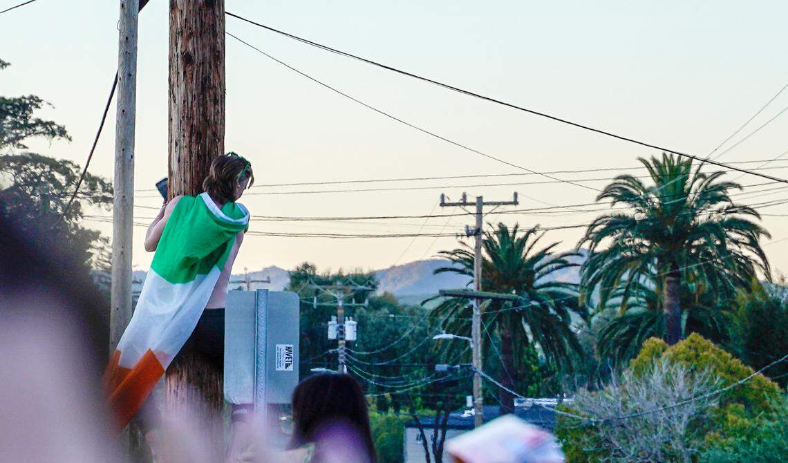 A person wearing an Irish flag attempts to climb a telephone pole at the St. Fratty’s Day party on Hathway Avenue near the university on March 16, 2024. A San Luis Obispo Police Department officer at the scene of the party estimated between 6,000 and 7,000 people in attendance.