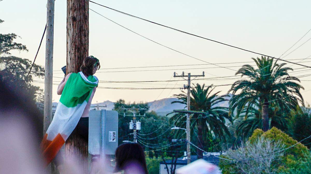 A person wearing an Irish flag attempts to climb a telephone pole at the St. Fratty’s Day party on Hathway Avenue near the university on March 16, 2024. A San Luis Obispo Police Department officer at the scene of the party estimated between 6,000 and 7,000 people in attendance.