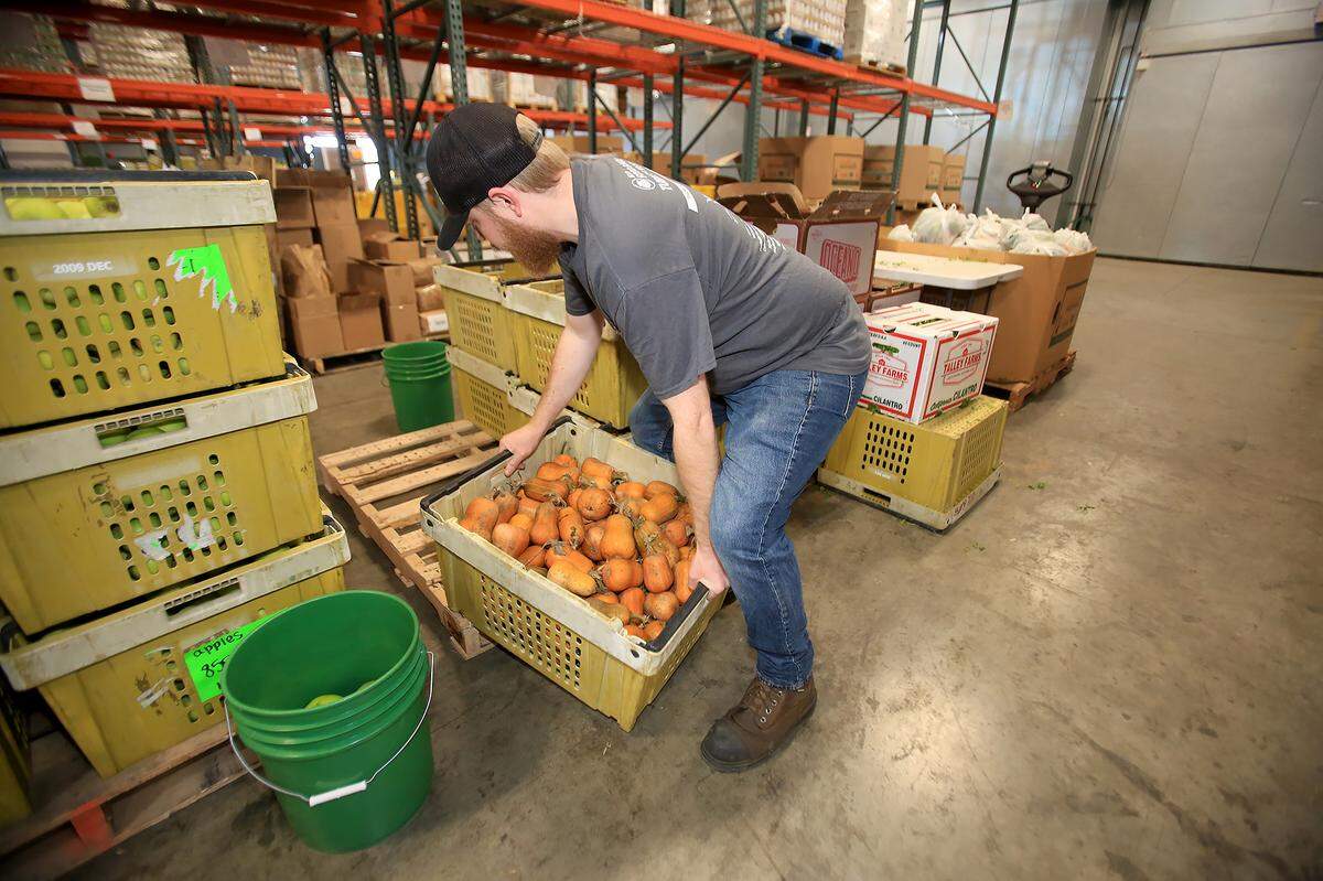 SLO Food Bank volunteers work stuffing plastic bags with food for needy persons. Inventory coordinator Andrew McCreery lifts a heavy box of fruit.
