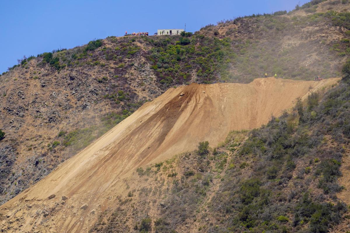 Dust rises from Regent’s Slide as Caltrans work teams clear debris from the slope, pictured Thursday, July 17, 2025. Regent’s Slide closed Highway 1 around 27 miles north of the San Luis Obispo-Monterey county line in February 2024.