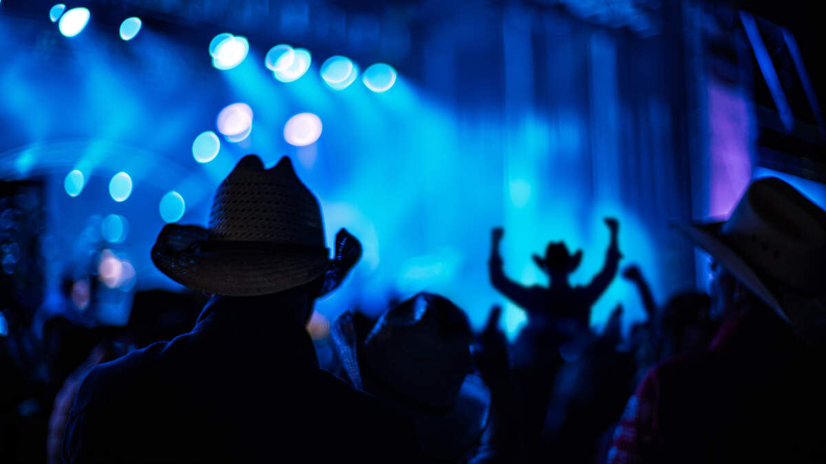 Silhouetted audience with cowboy hats at a country music concert under dynamic blue lighting.