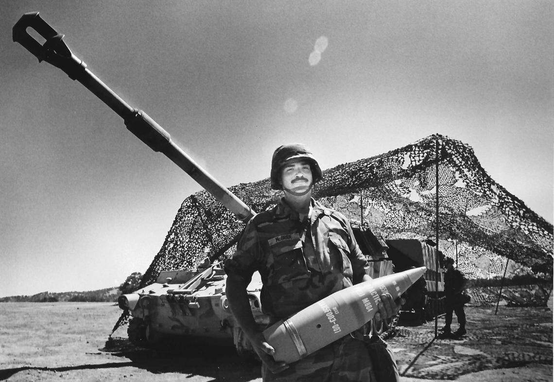 Sgt. Robert McBride holds 98-pound practice shell used in training at Camp Roberts. Behind him is a self-propelled 155 mm howitzer. Photo published Aug. 9, 1989.