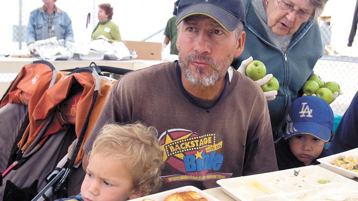 Ed Brecht and sons Malachi, 1, left, and Peter, 3, have lunch Thursday as Betty Ashton offers them apples at the South County People's Kitchen location on 16th Street in Grover Beach. Brecht said he's been homeless since being evicted in July.
