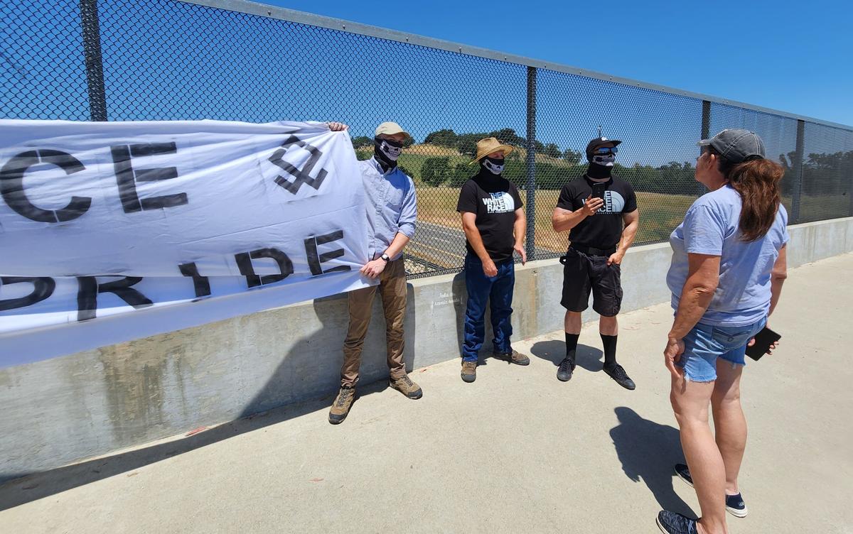 Several men with masks hold up an “Embrace white pride” flag on the Vineyard Drive Highway 101 overpass on Saturday, May 13, 2023.